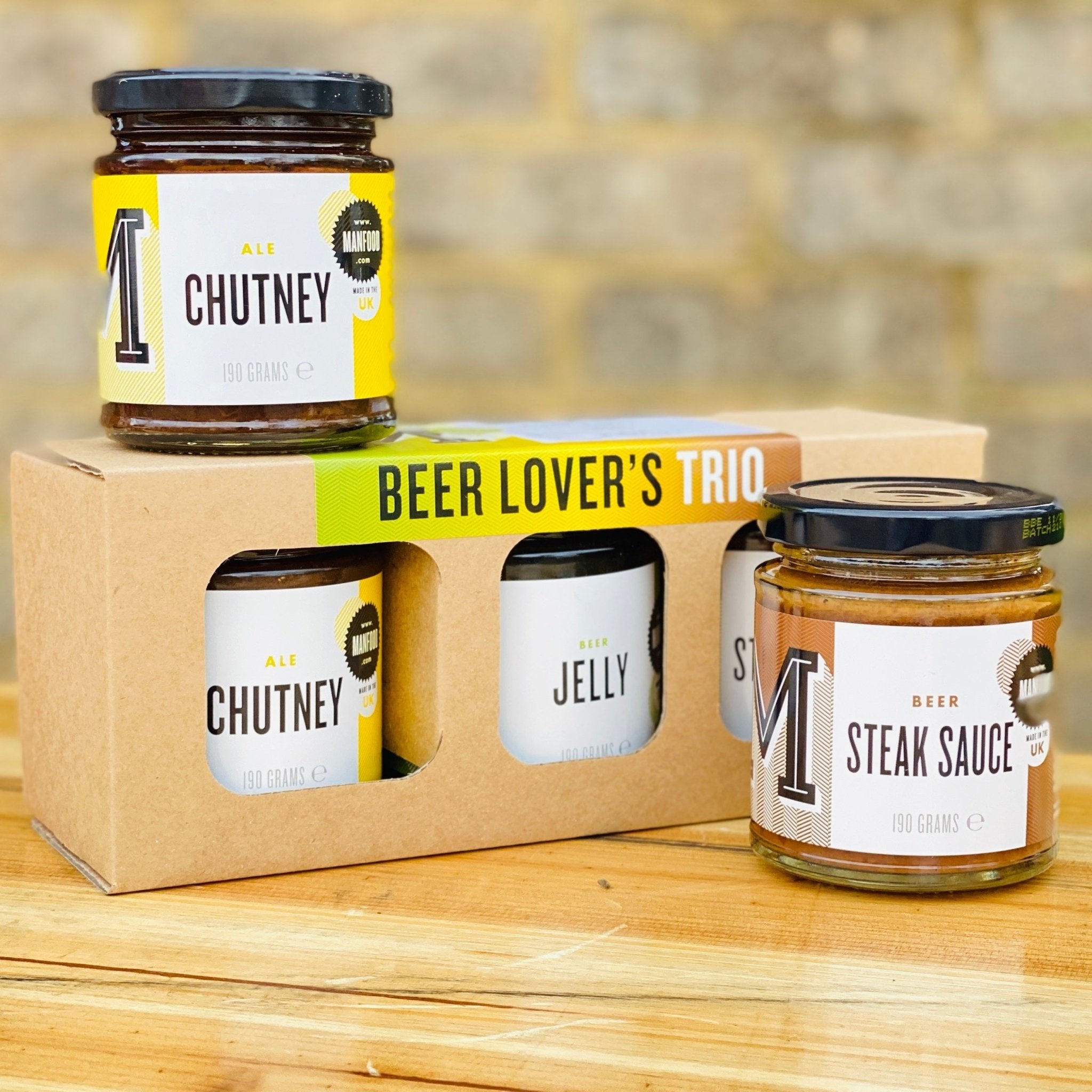 Three jars of different condiments in a 'Beer Lover's Trio' packaging on a wooden surface. Gifts for dad. Stocking Filler